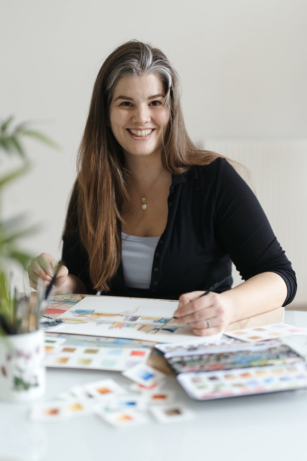 Portraitfoto-Anna-Just_mit-Blick-über-den-Arbeitstisch-laechelnd-in-die-Kamera_photocredits-charlotte-jani