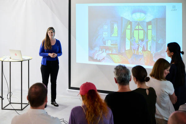 Anna Just, in kobaltblau, präsentiert ihre aktuellen Arbeiten  vor den österreichischen Verlagshäusern. im Designforum Austria. Via Beamer sieht man das Bild "Oh Tante Petunia" und dazu erzählt sie von ihrem Verständnis von Raum und Licht in ihren Bildern.
